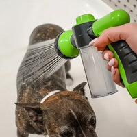 A wet dog being rinsed with water from a handheld green and black spray nozzle attached to a clear water container, held by a person in a white bathroom setting.